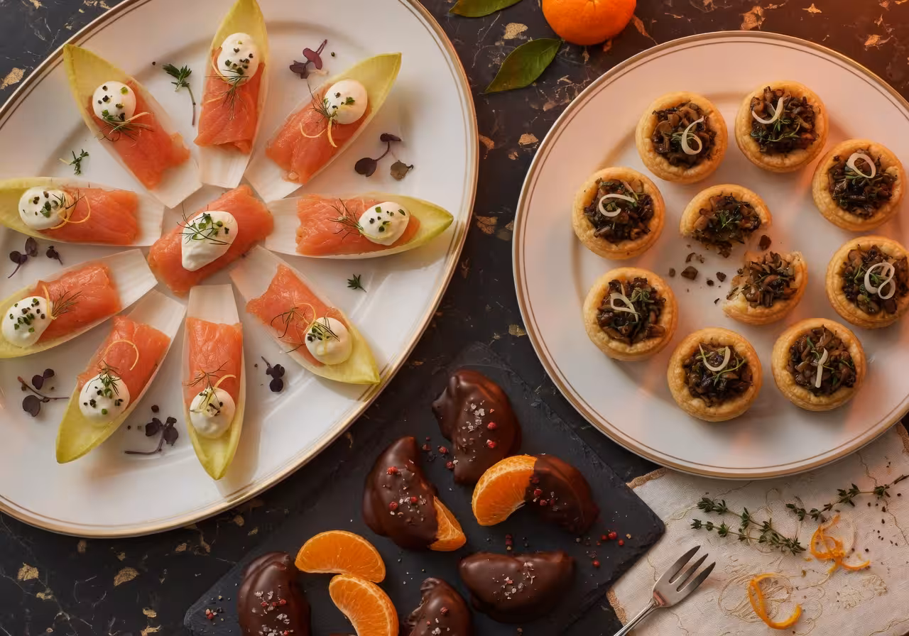 elegant holiday appetizers arranged on serving platters, smoked salmon on endive leaves with crème fraîche and dill, and mushroom puff pastry bites
